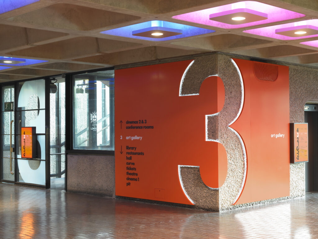 Large interior corner sign with a "3" carved out with back lighting glowing from within the number. Has wayfinder directions on the large illuminated orange sign.